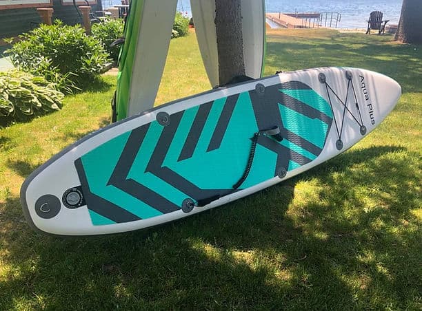 Stand-up paddleboard resting on grass near the waterfront.